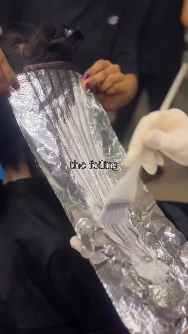 A colourist brushing lightener onto a section of hair laid over foil